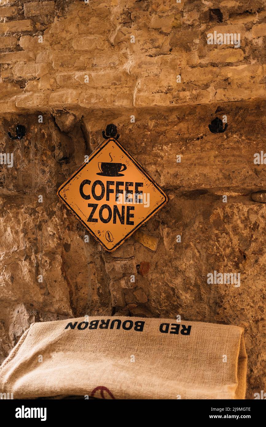 Coffee Zone sign hanging on aged rough stone wall over sack with Red Bourbon inscription in cozy cafe Stock Photo