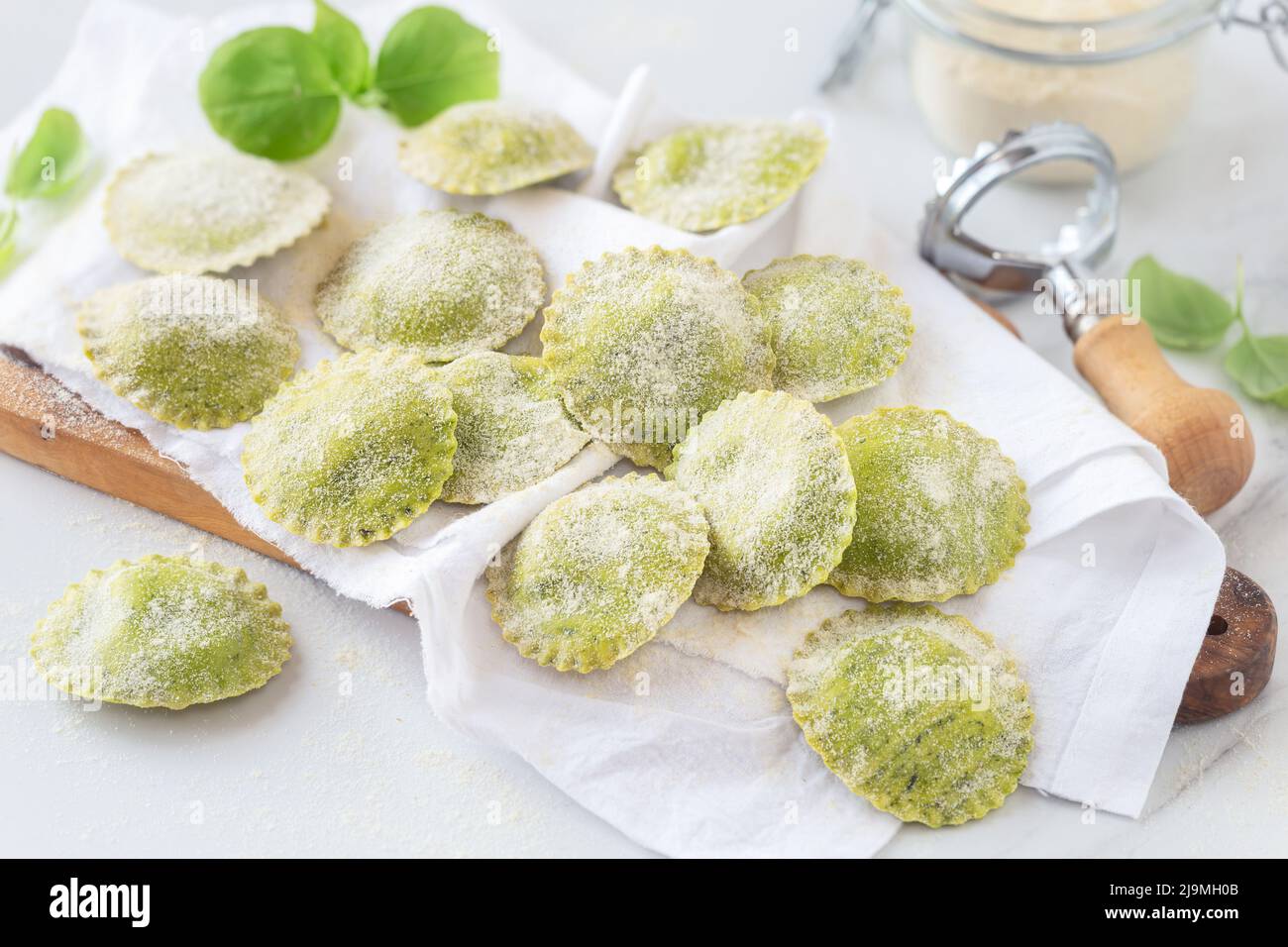 Fresh homemade ravioli with basil dough placed on napkin on wooden cutting board Stock Photo