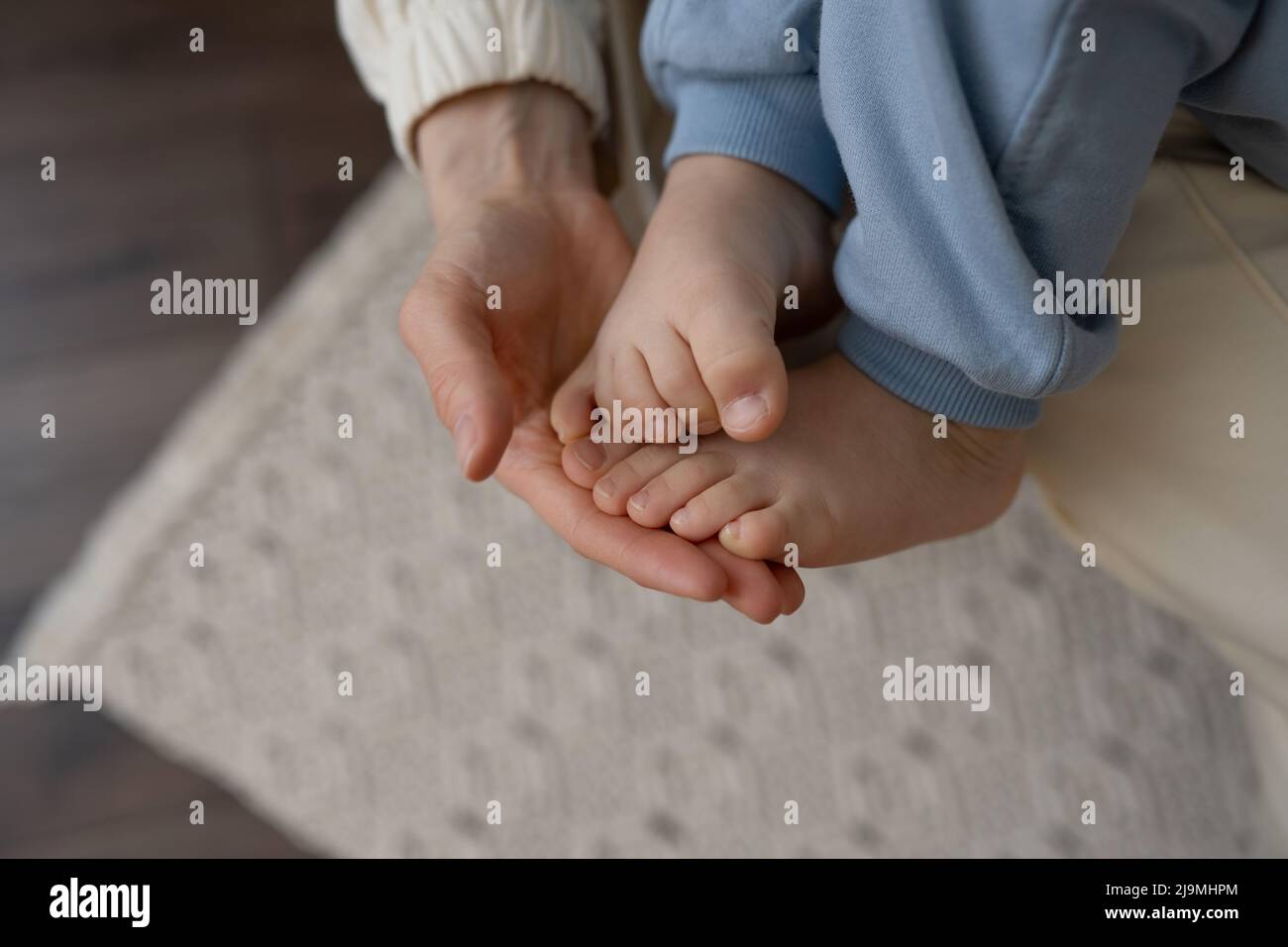 From above of crop unrecognizable mother touching bared foot of anonymous kid sitting on floor at home Stock Photo
