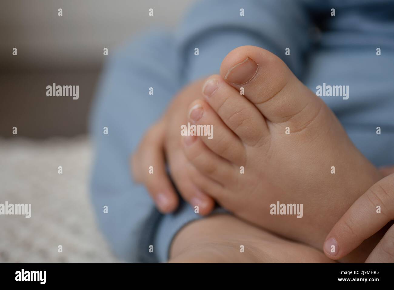 Closeup of crop unrecognizable little kid touching bared feet while sitting on carpet on floor at home Stock Photo