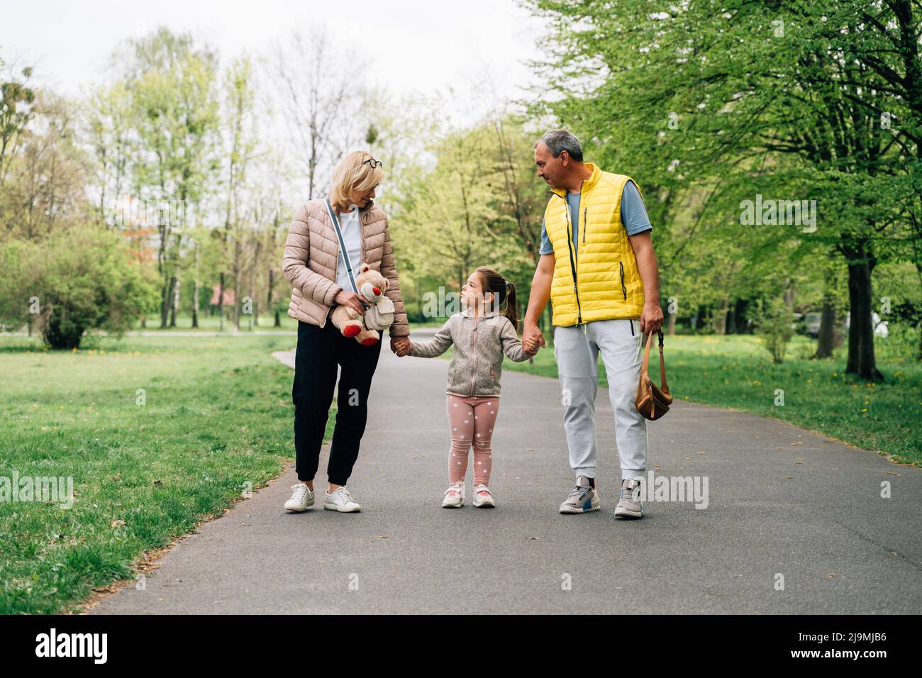 Mature grandparents in casual clothes holding hands of adorable happy