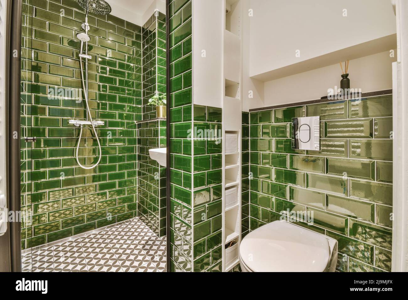 Shower cabin placed at green tiled wall near sink and toilet in light