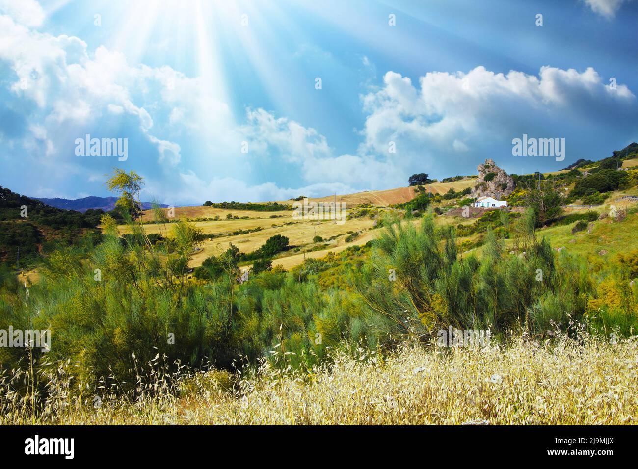 Typical andalusian calm mountain valley landscape, sun rays, low morning clouds, idyllic white farm house in rock front, agricultural fields - Spain, Stock Photo