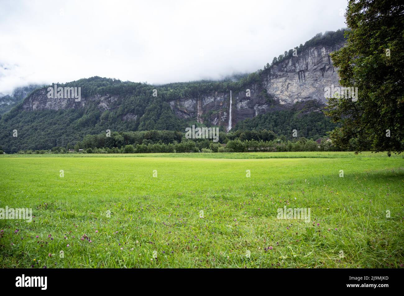 Panoramic view of Reichenbach falls on mountains overlooking the lush green meadows captured from the country side village of Meiringen, Switzerland Stock Photo