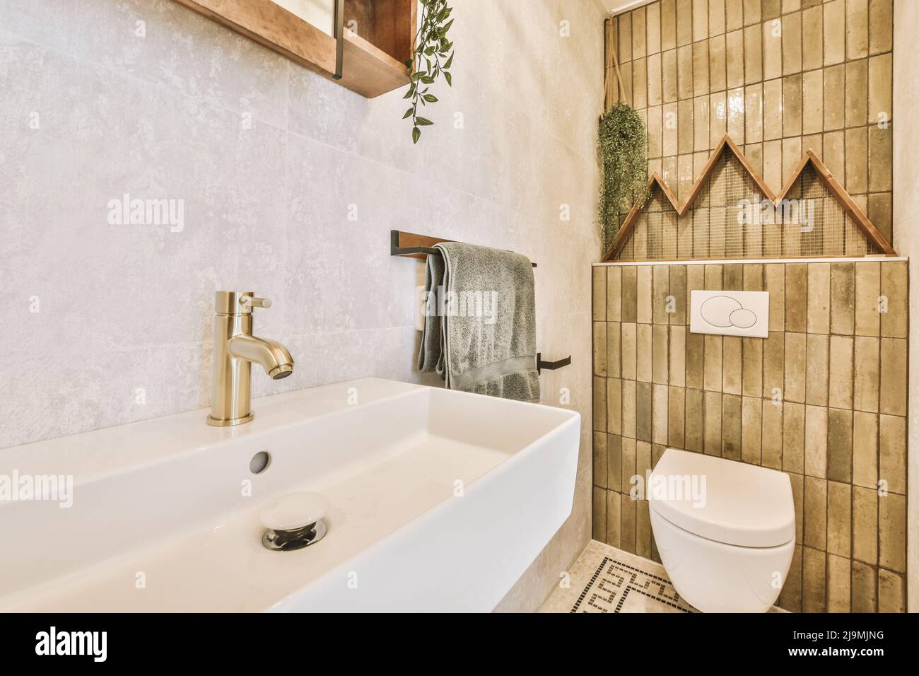 Ceramic sink with golden faucet installed on tiled wall with mirror