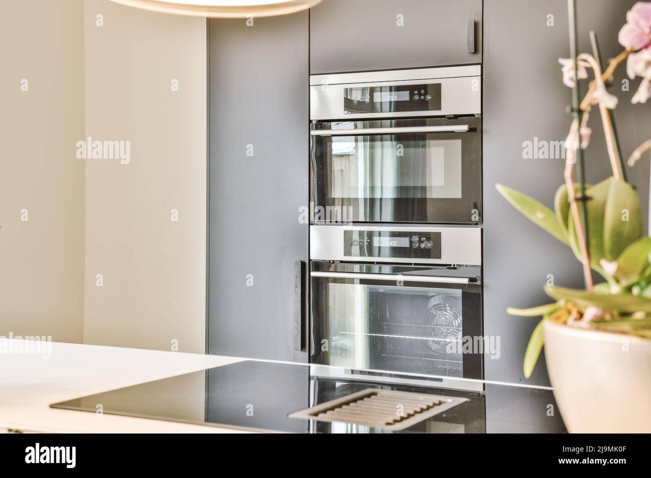 Modern built in ovens installed into gray cupboards behind counter in sunlit kitchen in daytime Stock Photo