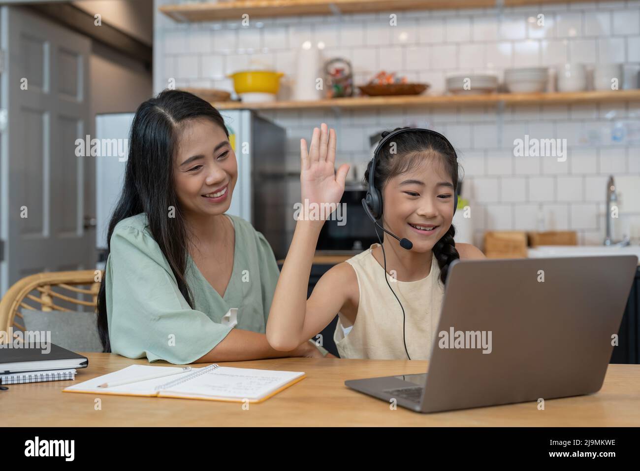 Happy asian mother and child sitting at kitchen table with colored pencils, attending virtual drawing class via video call, smiling and waving hello Stock Photo