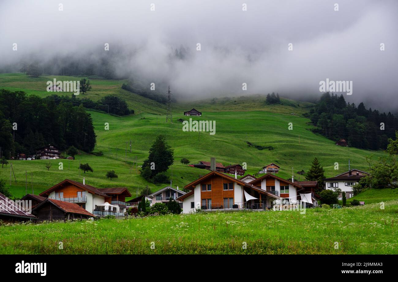 View of a red wooden chalet farm house surrounded by mountains and green meadows, alongside the lake Lungern situated at the alpine village of Lungern Stock Photo