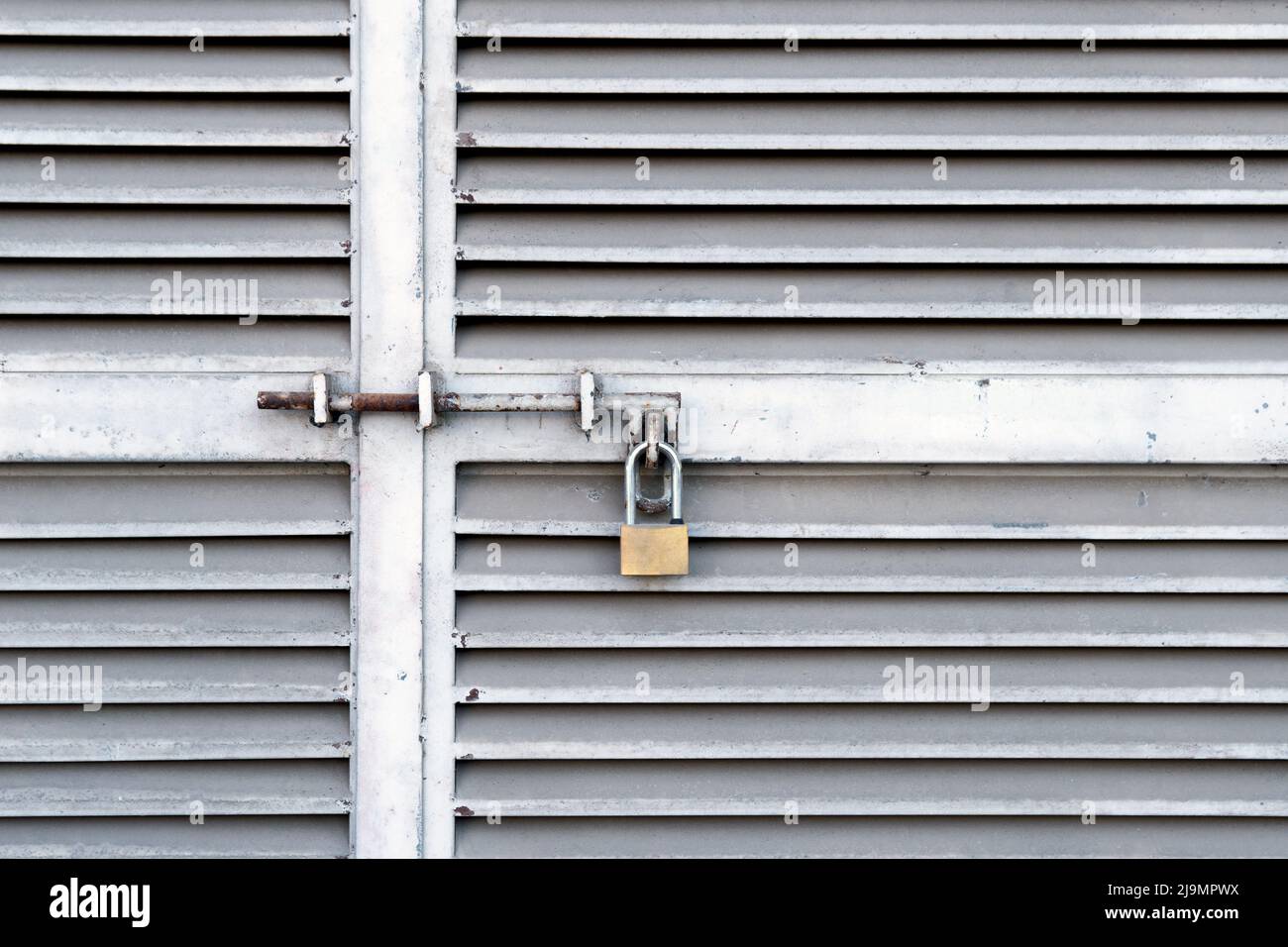 Small padlock hanging on closed metal doors Stock Photo