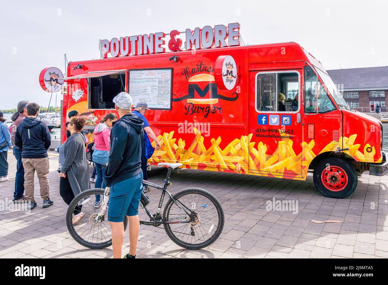 People are by a Poutine food truck which is parked in the waterfront district. Stock Photo