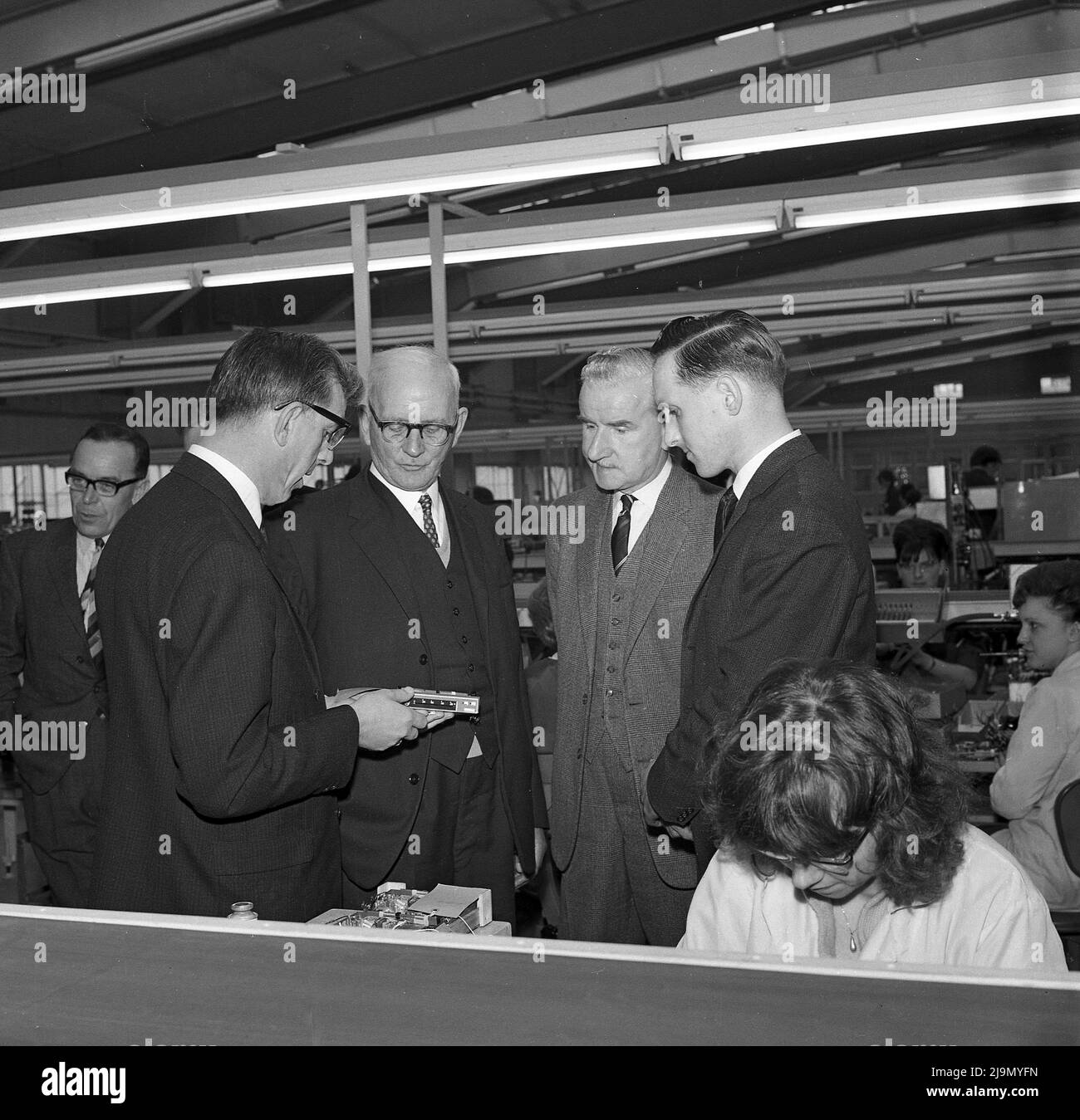 1960s, historical, company directors on the factory floor where workers are producing components for Philips radio sets. Philips was a pioneer in the field of radio sets and transistors, launched its first electronic tubes (radio components) and marketed its first radios in 1927. Stock Photo