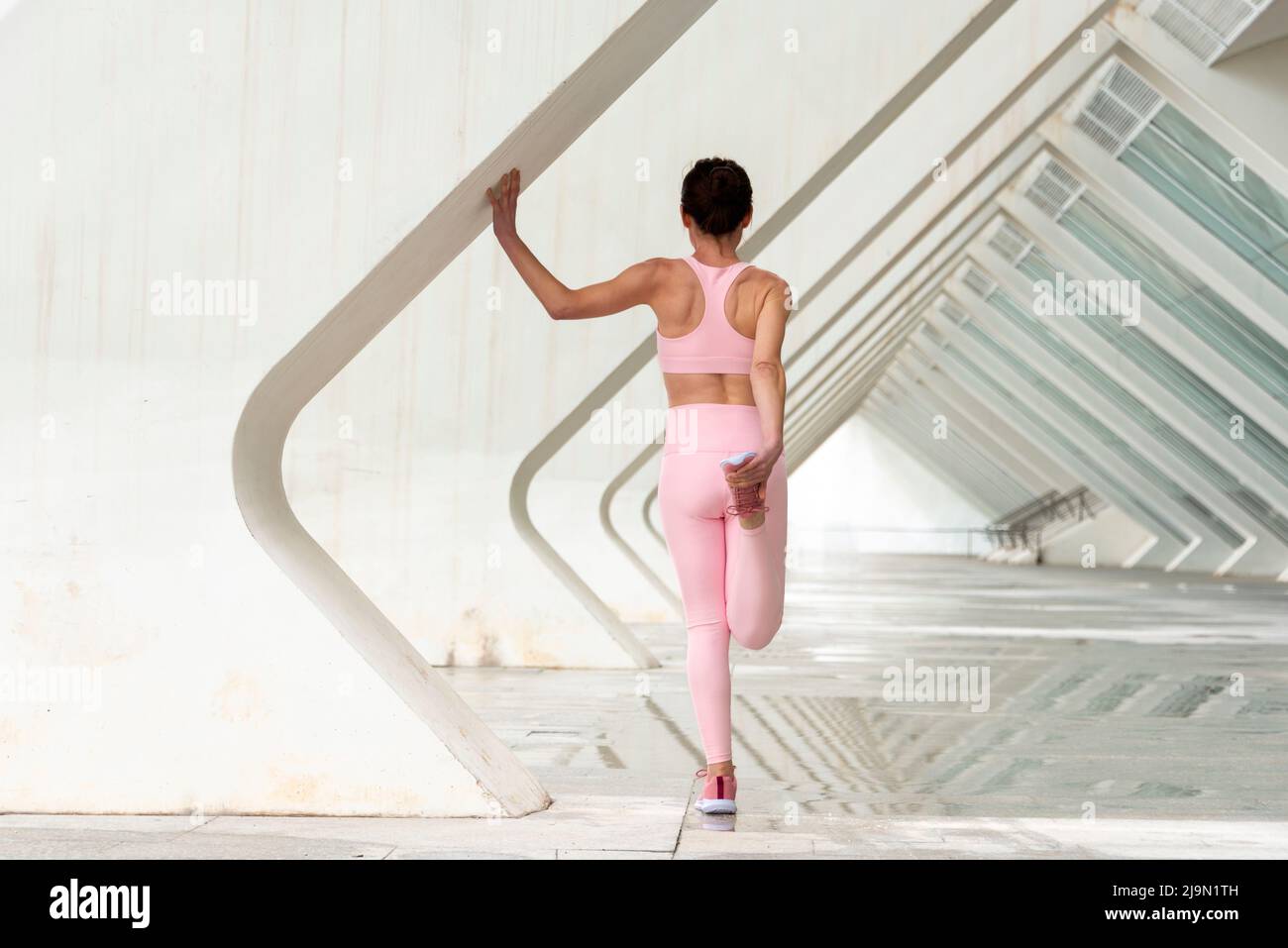 rear view of a sporty woman doing a leg stretch warm up exercise before running, urban background. Stock Photo