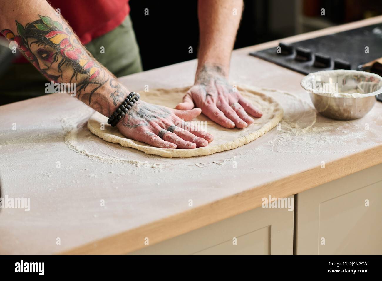 Unrecognizable tattooed man standing at kitchen counter kneading and