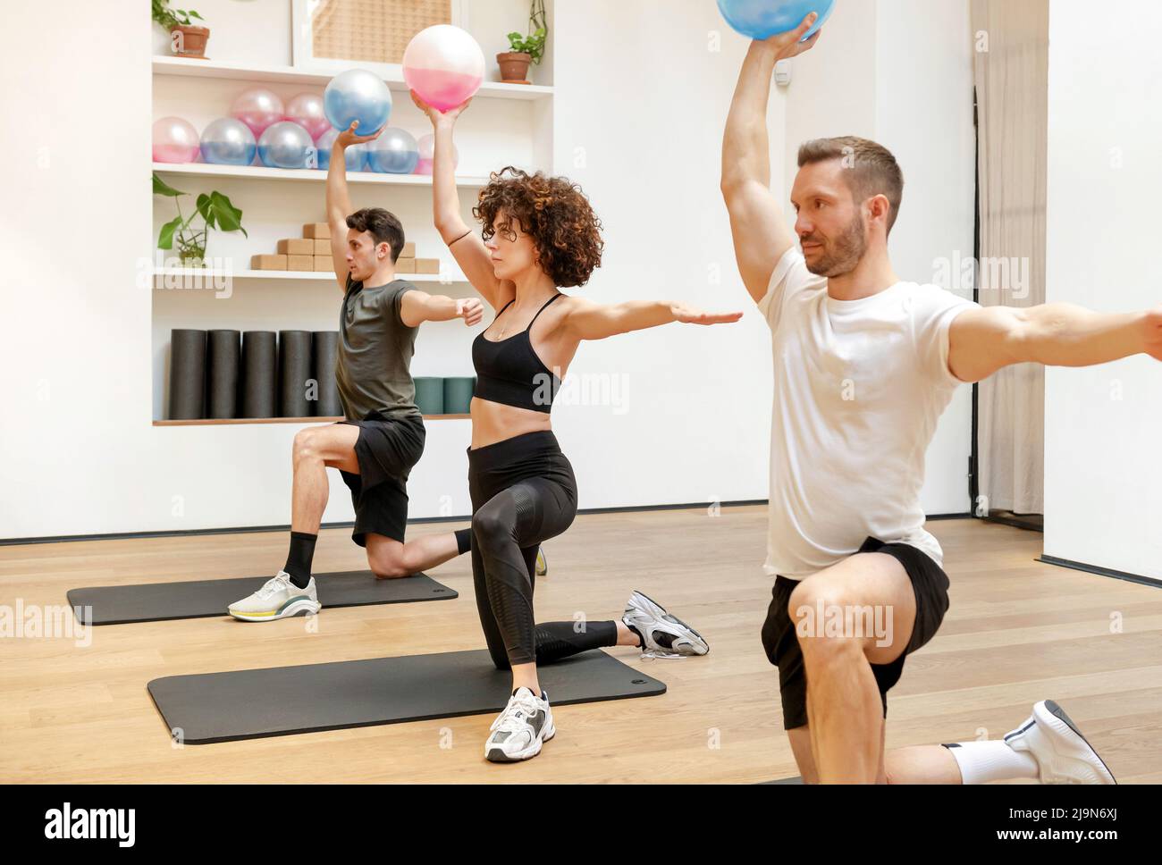 Group of focused sportive people in activewear doing shoulder press exercise with medicine ball filled with fluid during fitness class Stock Photo