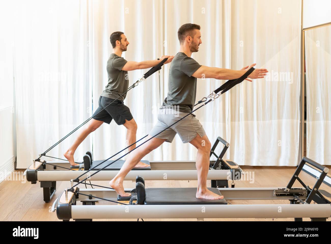 Side view full body of athletic males doing tree hugs exercise while standing on reformers during pilates class Stock Photo