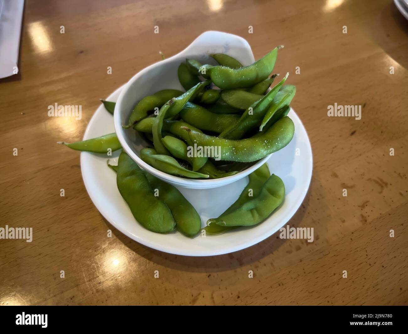Close up, selective focus on edamame pods in a small white cup on a wooden table inside a restaurant Stock Photo