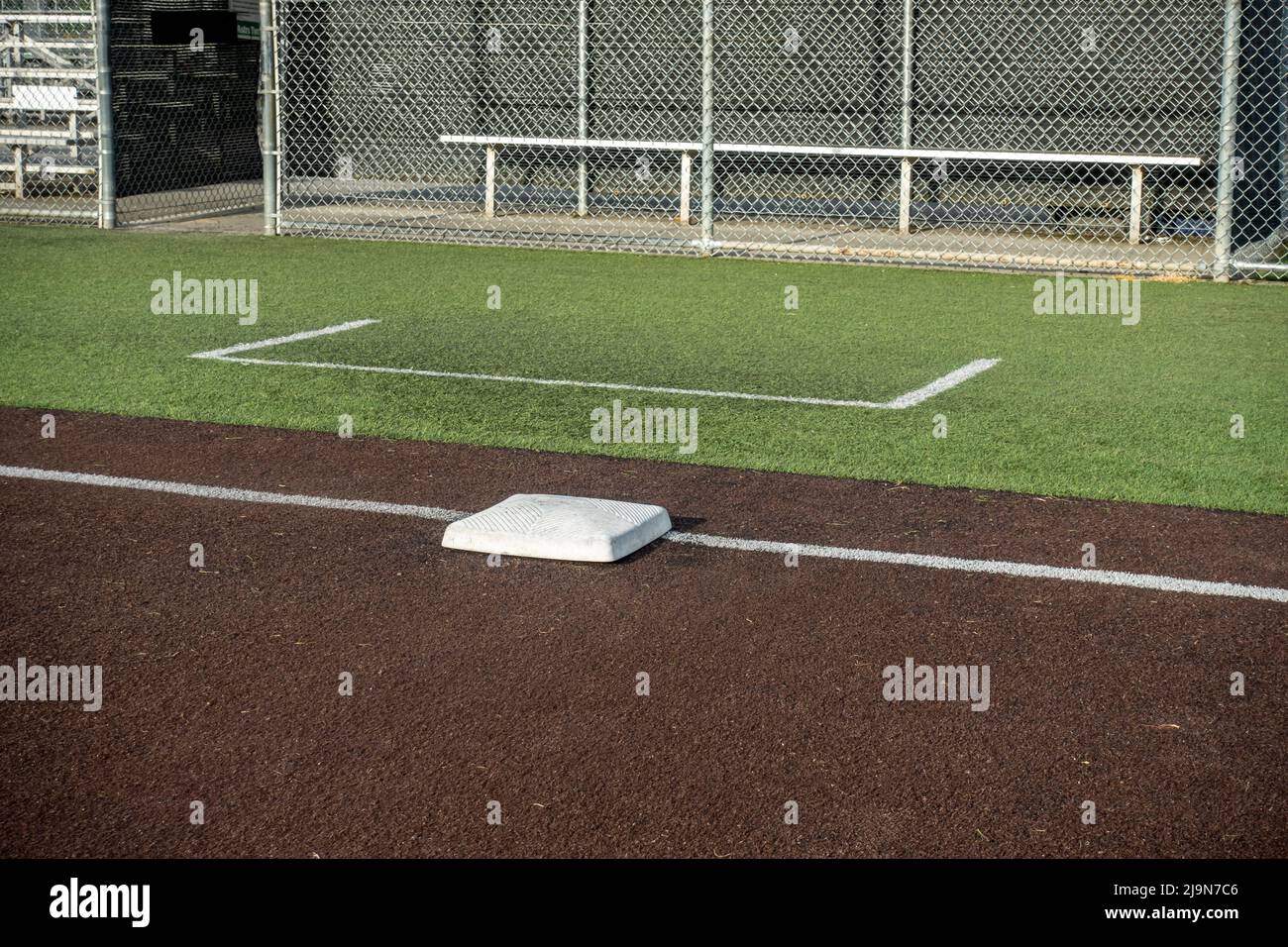 Angled view of a white base on a baseball field, with the view of a dugout in the background Stock Photo