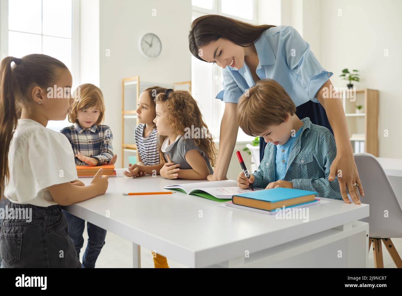 Friendly female teacher helping little boy with test assignments in classroom at elementary school. Stock Photo
