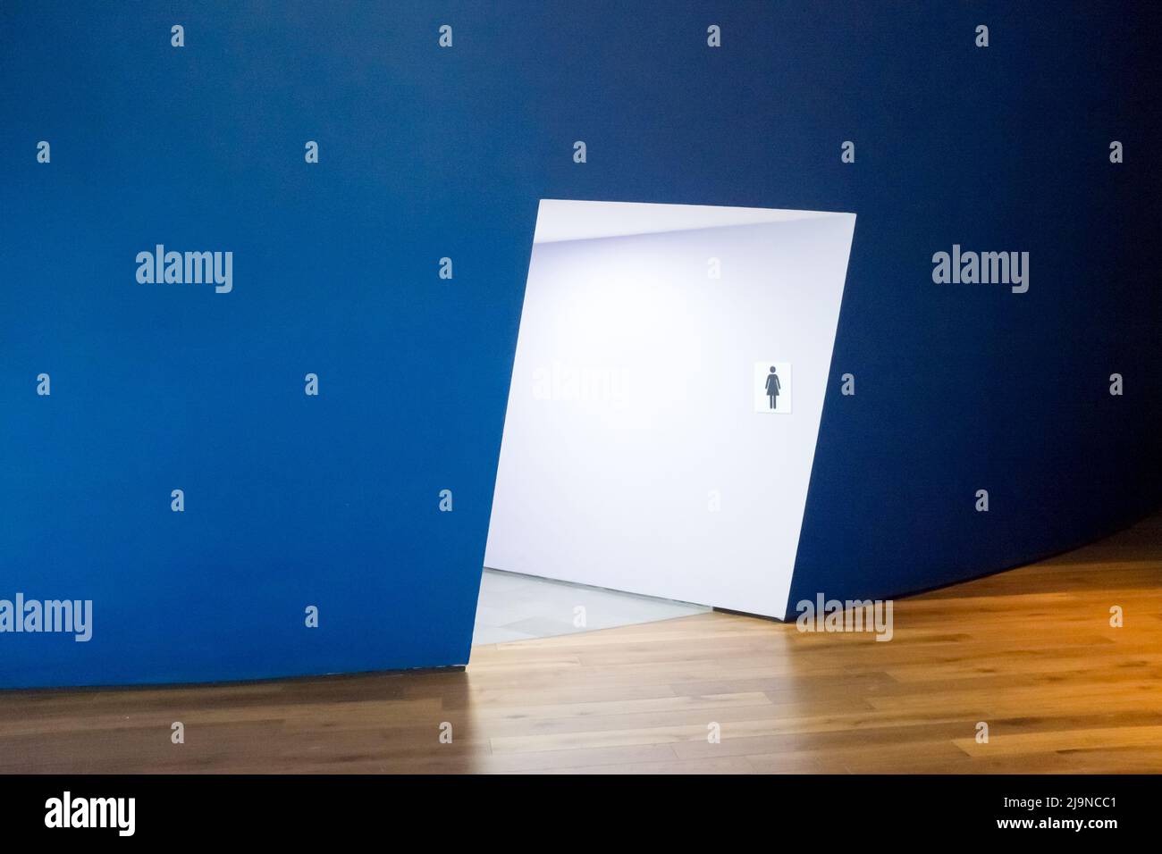 Interior architecture of a blue curved wall and illuminated slanted passageway leading to a female public toilet entrance at the Firesite Art Gallery Stock Photo