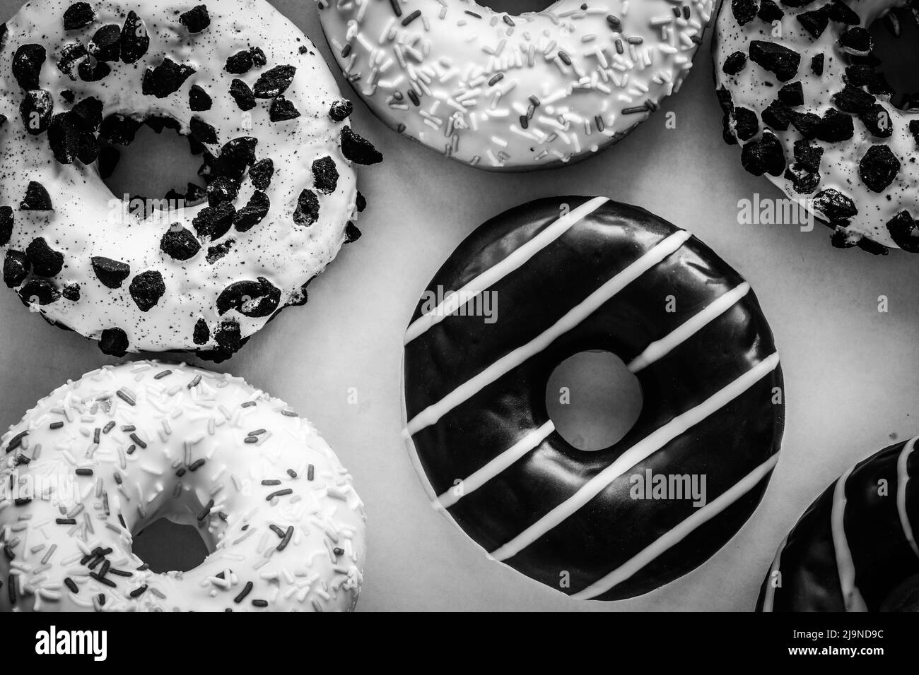 Flat lay image of donut with chocolate glaze with stripes amids other different donuts - black and white image Stock Photo