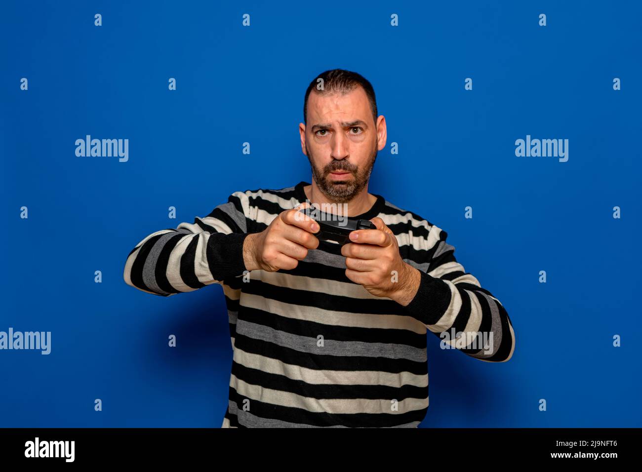 Portrait of concentrated bearded Caucasian man playing video games with a controller in his hands, isolated on blue studio background Stock Photo