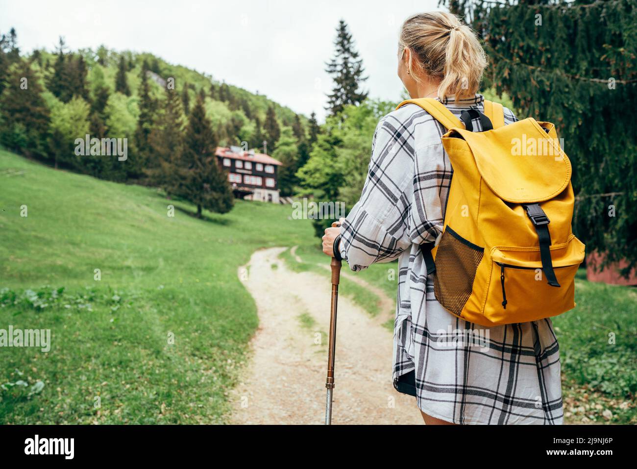 Lonely female with yellow backpack walking by mountain path with trekking poles to mount refuge hut in Slovakia, Mala Fatra region. Active people and Stock Photo