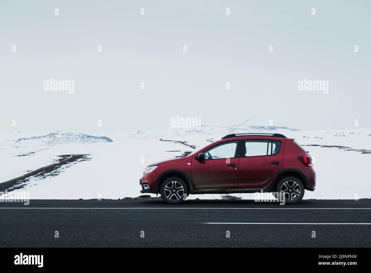 Kars, Turkey - February 25, 2022: Side view of a red colored Dacia brand Sandero model car paused on an asphalt road with a snowy background. Stock Photo