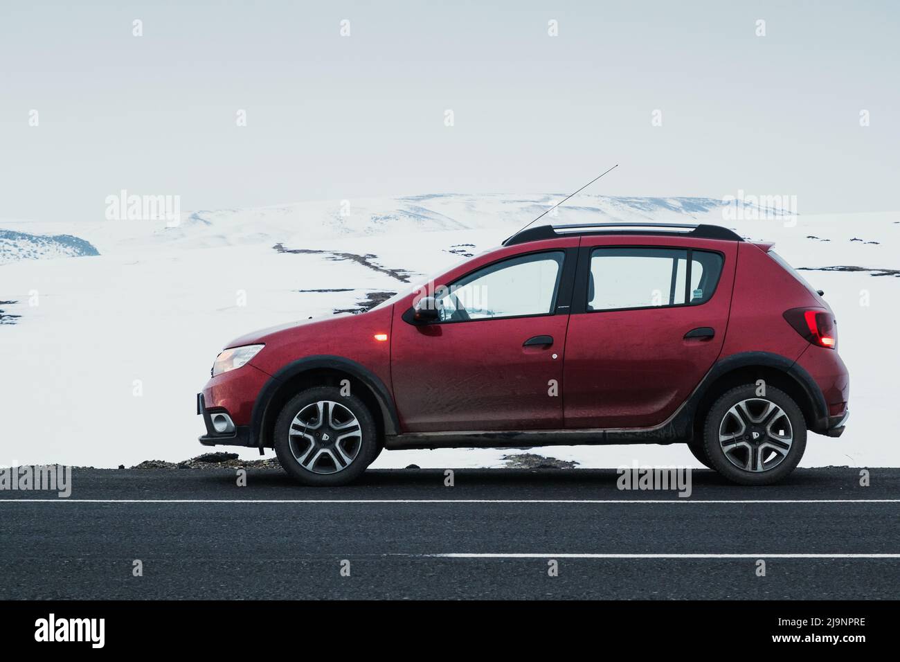 Kars, Turkey - February 25, 2022: Side view of a red colored Dacia brand Sandero model car paused on an asphalt road with a snowy background. Stock Photo