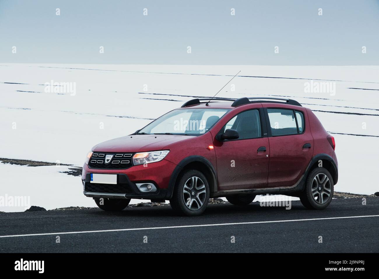 Kars, Turkey - February 25, 2022: Front and side view of a red colored Dacia brand Sandero model car paused on an asphalt road with a snowy background Stock Photo