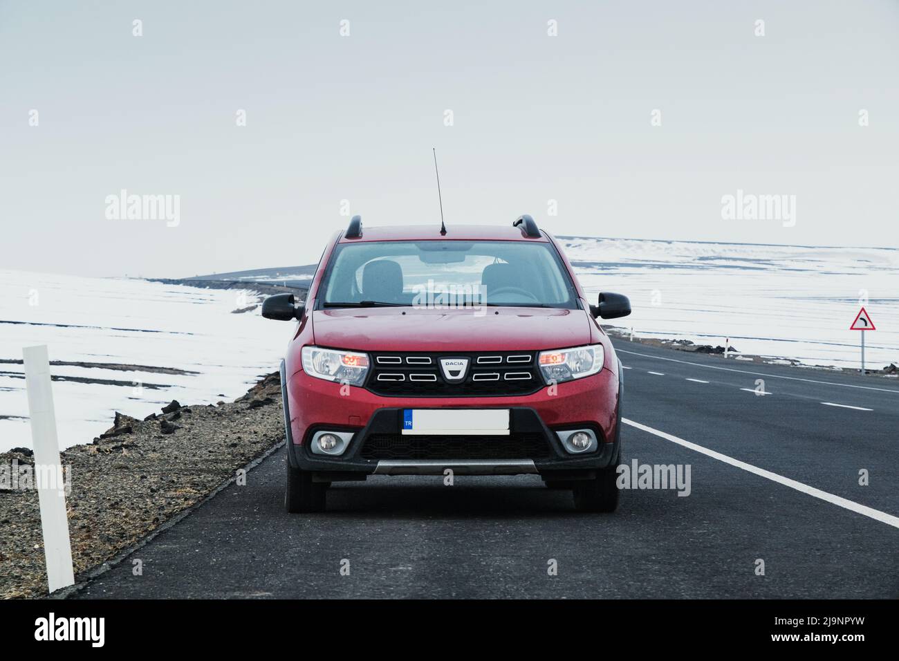 Kars, Turkey - February 25, 2022: Front view of a red colored Dacia brand Sandero model car paused on an asphalt road with a snowy background. Stock Photo