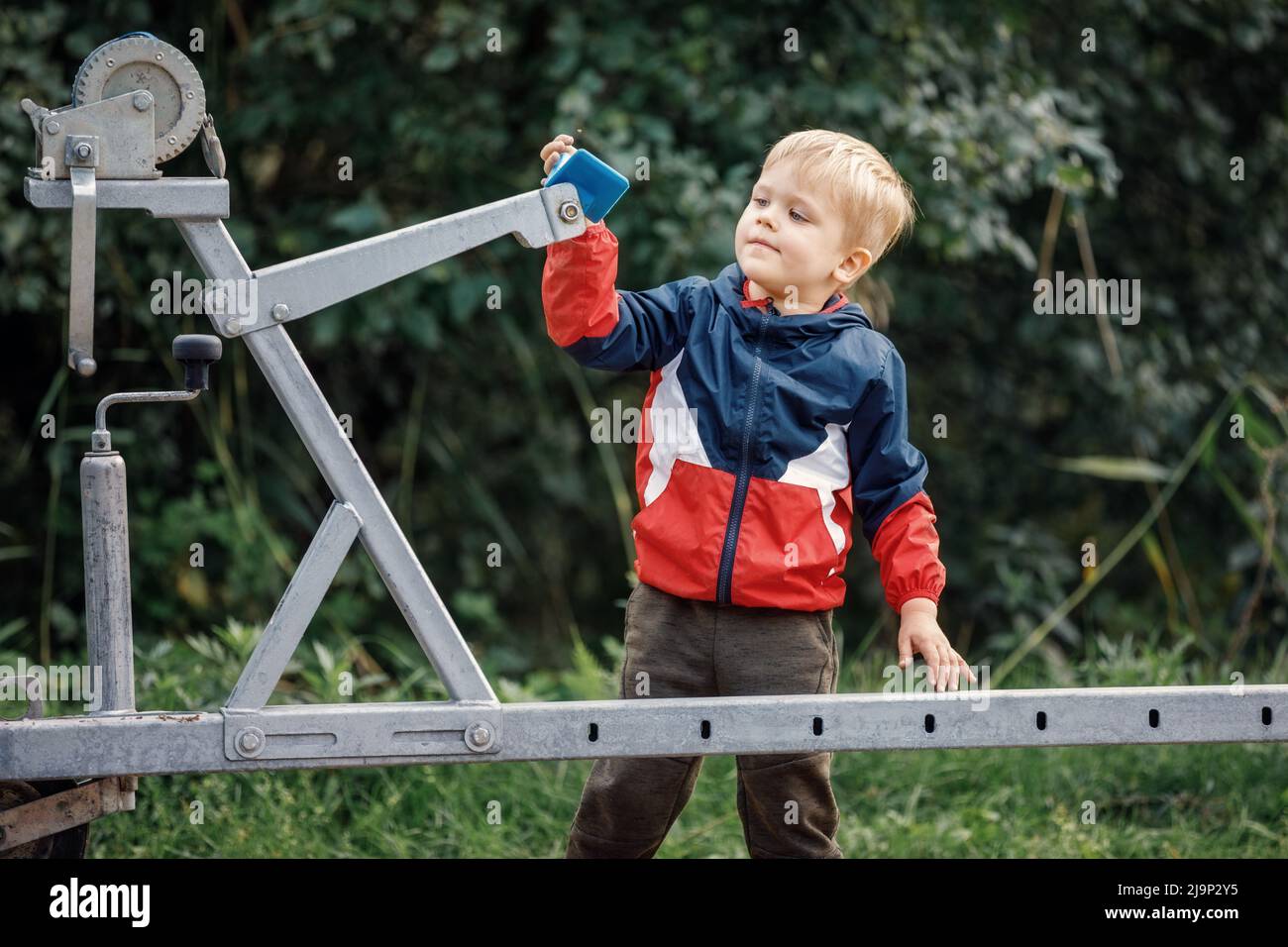 The curious little boy researching boat trailer clutch system in nature foliage background. Stock Photo