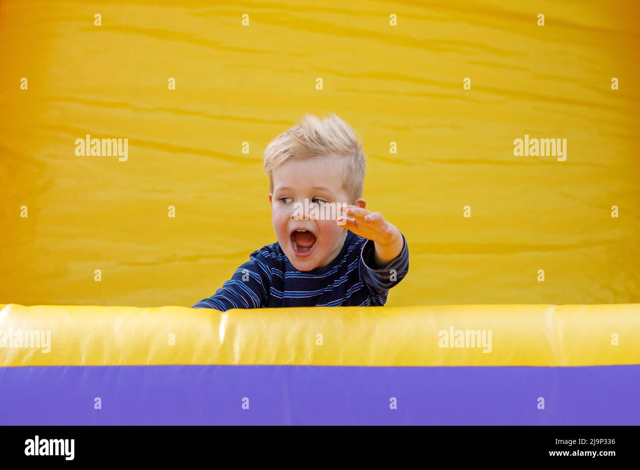 A child is happy and shouts on an inflatable yellow playground. Amusement park for children. Inflatable trampoline for jumping and fun. Rest in the su Stock Photo