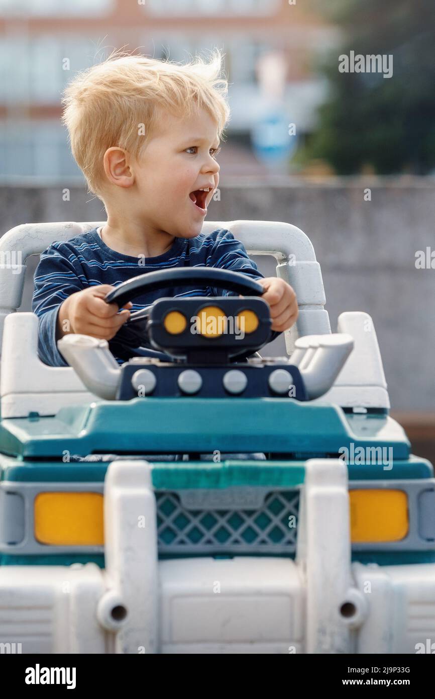Close up portrait of young happy kid driving electric toy car outdoors. Stock Photo