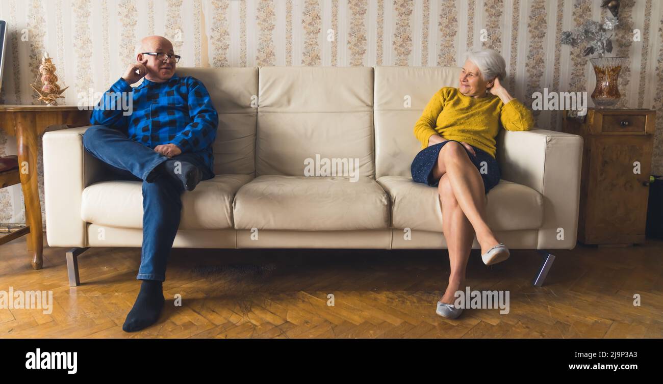 happy Caucasian grandparents sitting apart at the opposite ends of the sofa full shot indoor senior people concept. High quality photo Stock Photo
