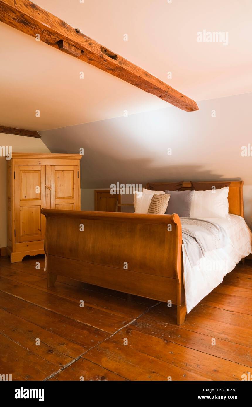 Antique sleigh bed and armoire in upstairs main bedroom inside old circa 1741 Canadiana cottage style home. Stock Photo