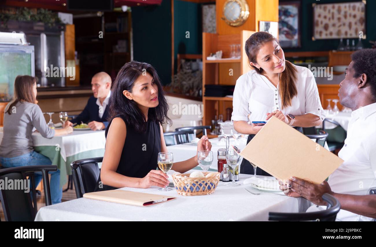 positive female busboy taking order to couple in modern restaurante Stock Photo