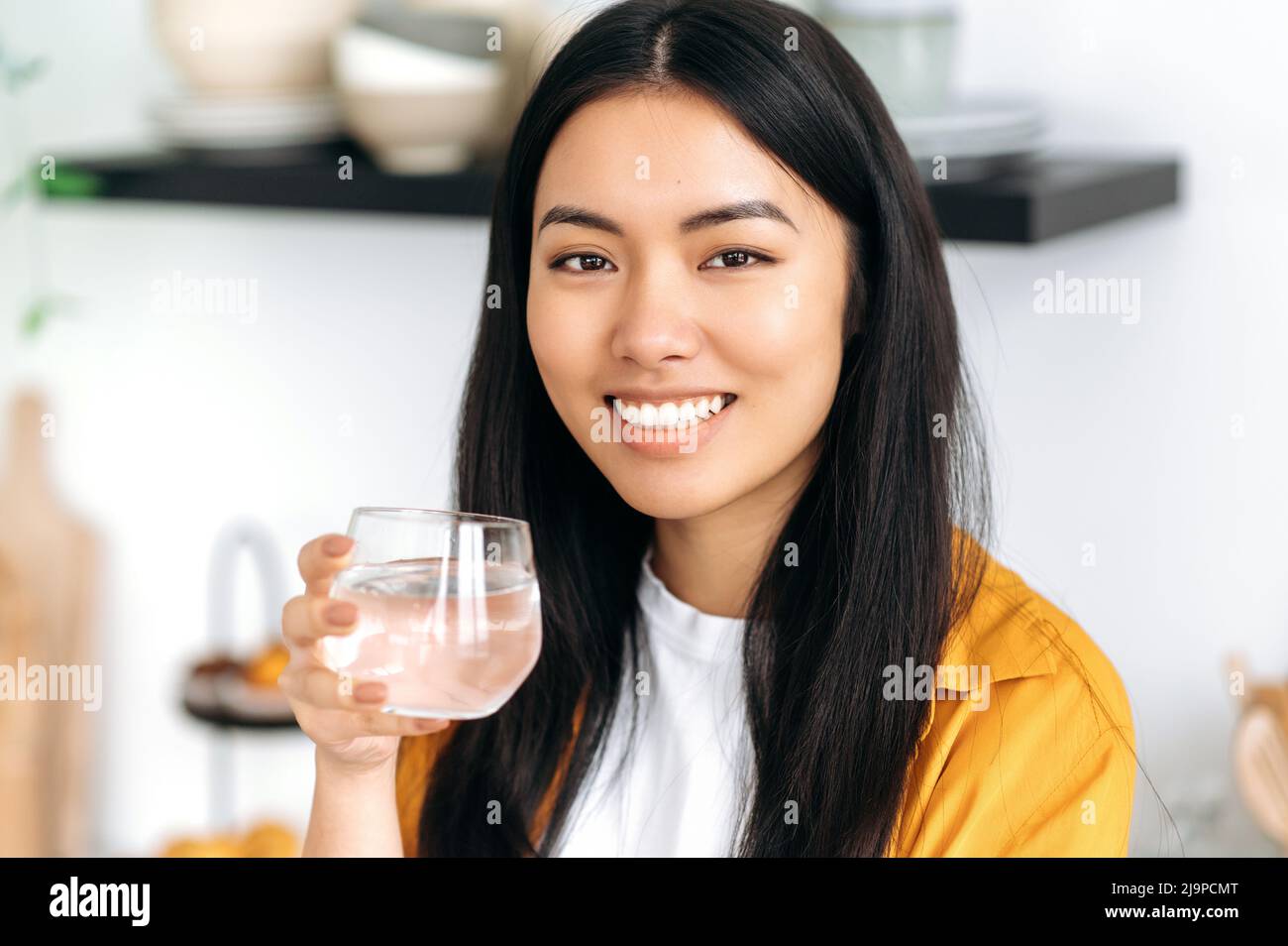 https://c8.alamy.com/comp/2J9PCMT/pretty-healthy-chinese-brunette-girl-dressed-in-casual-stylish-clothes-holds-a-glass-of-pure-water-takes-care-of-her-health-drinks-daily-norm-of-water-looking-at-camera-smiles-friendly-2J9PCMT.jpg