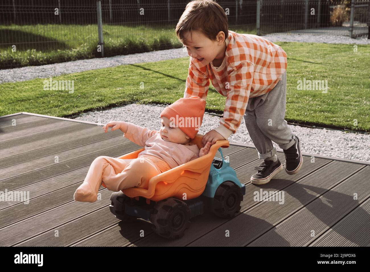 Brother giving a ride to baby sister in big toy car outdoors. Children