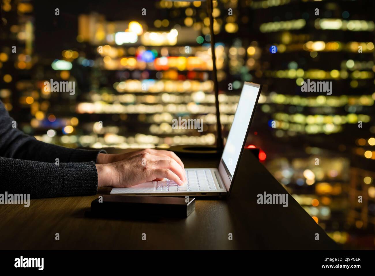 Working with computer at night, out focus city skyline background Stock Photo