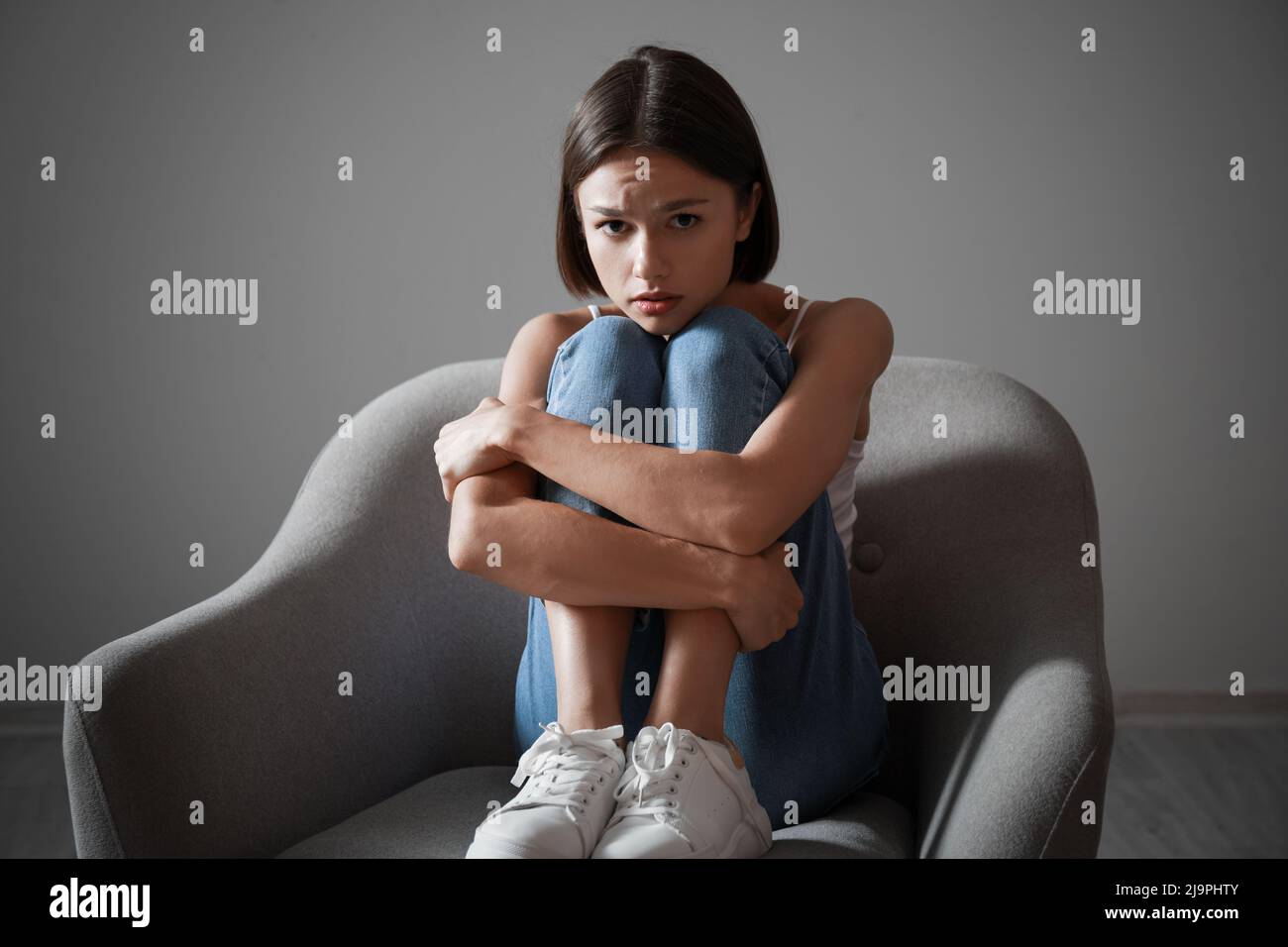 Sad young woman sitting in armchair at home. Violence concept Stock