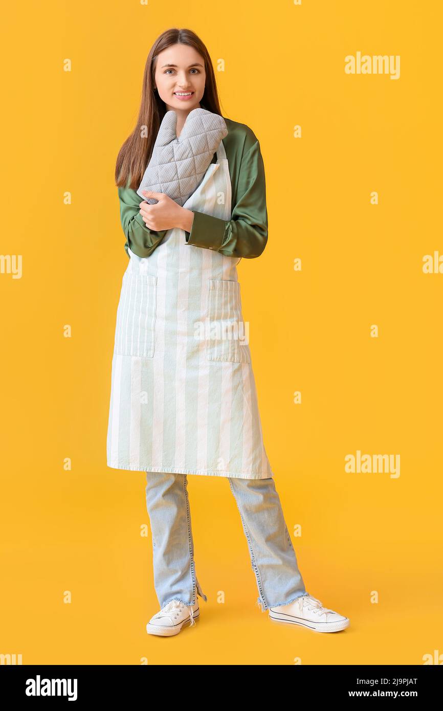 Pretty young woman with oven mitten on yellow background Stock Photo
