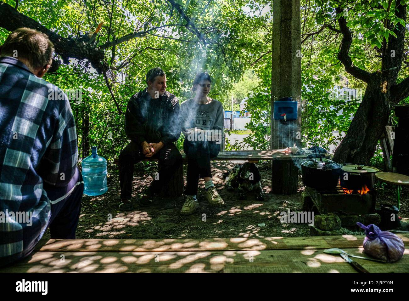 People seat under the trees and cook food near the entrance of a bunker in the outskirts of the city. Lysychansík, Luhansk region. 23 May 2022 Lysychansk is an elongated city on the high right bank of the Donets River in the Luhansk region. The city is part of a metropolitan area that includes Severodonetsk and Rubizhne; the three towns together constitute one of Ukraine's largest chemical complexes. The town is about 7 km from the frontline, and Russian troops are moving towards it, the city, like Severodonetsk, is almost isolated. Russian are trying to occupy the main road that connect Lysy Stock Photo