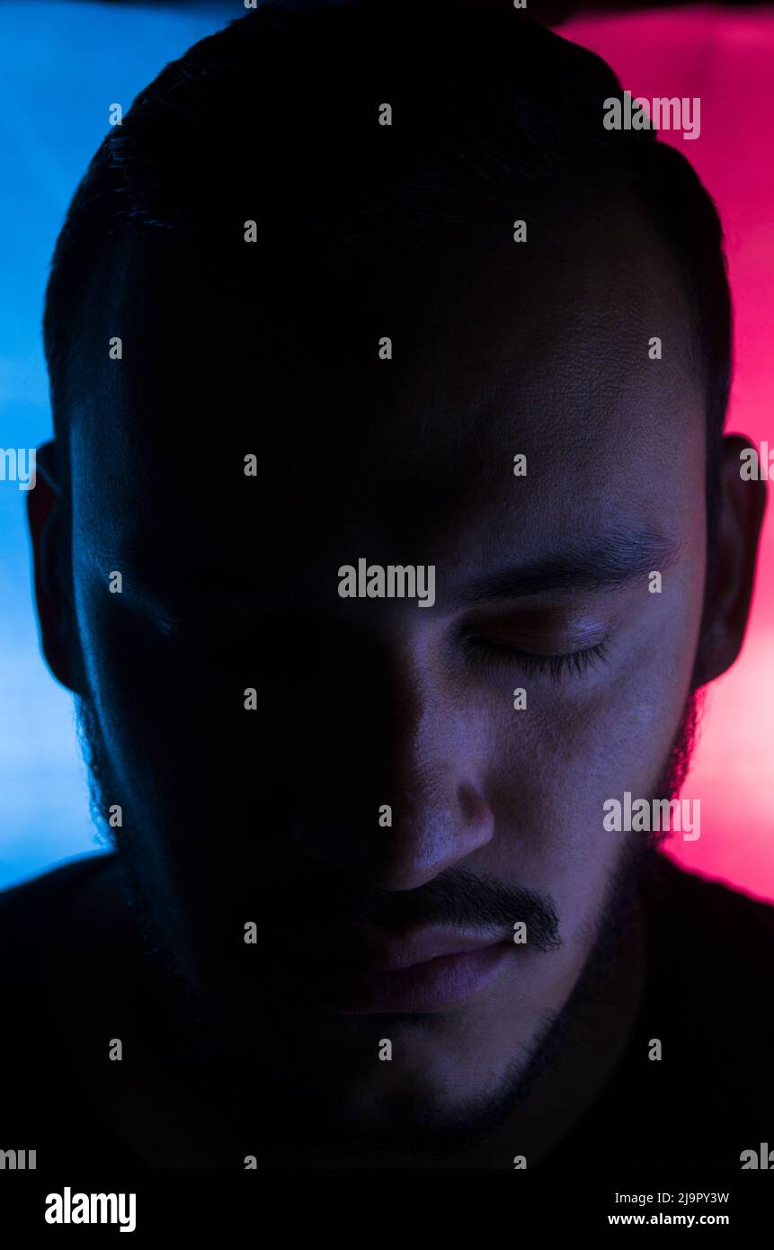Portrait of man with closed eyes and blue and red background. Tilted