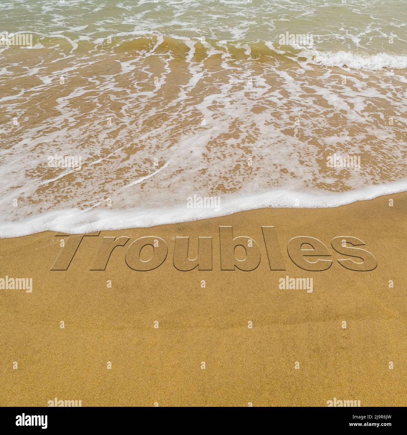 Concept image - to illustrate washing away stress by taking a vacation as waves on a sandy beach wash away the word 'troubles'. Stock Photo