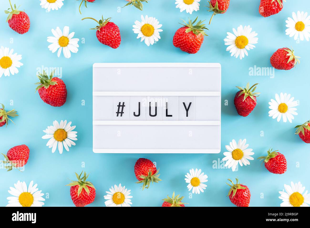Summer month July text on light box and strawberry, chamomile flowers on blue background. Creative concept Hello July. Top view, Flat lay, greeting ca Stock Photo