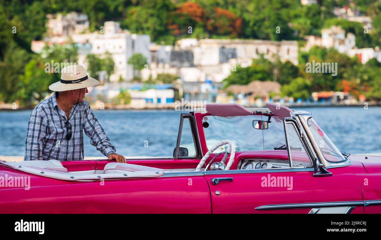 Cuban taxi driver standing by his vintage American car and waiting for tourists. Stock Photo
