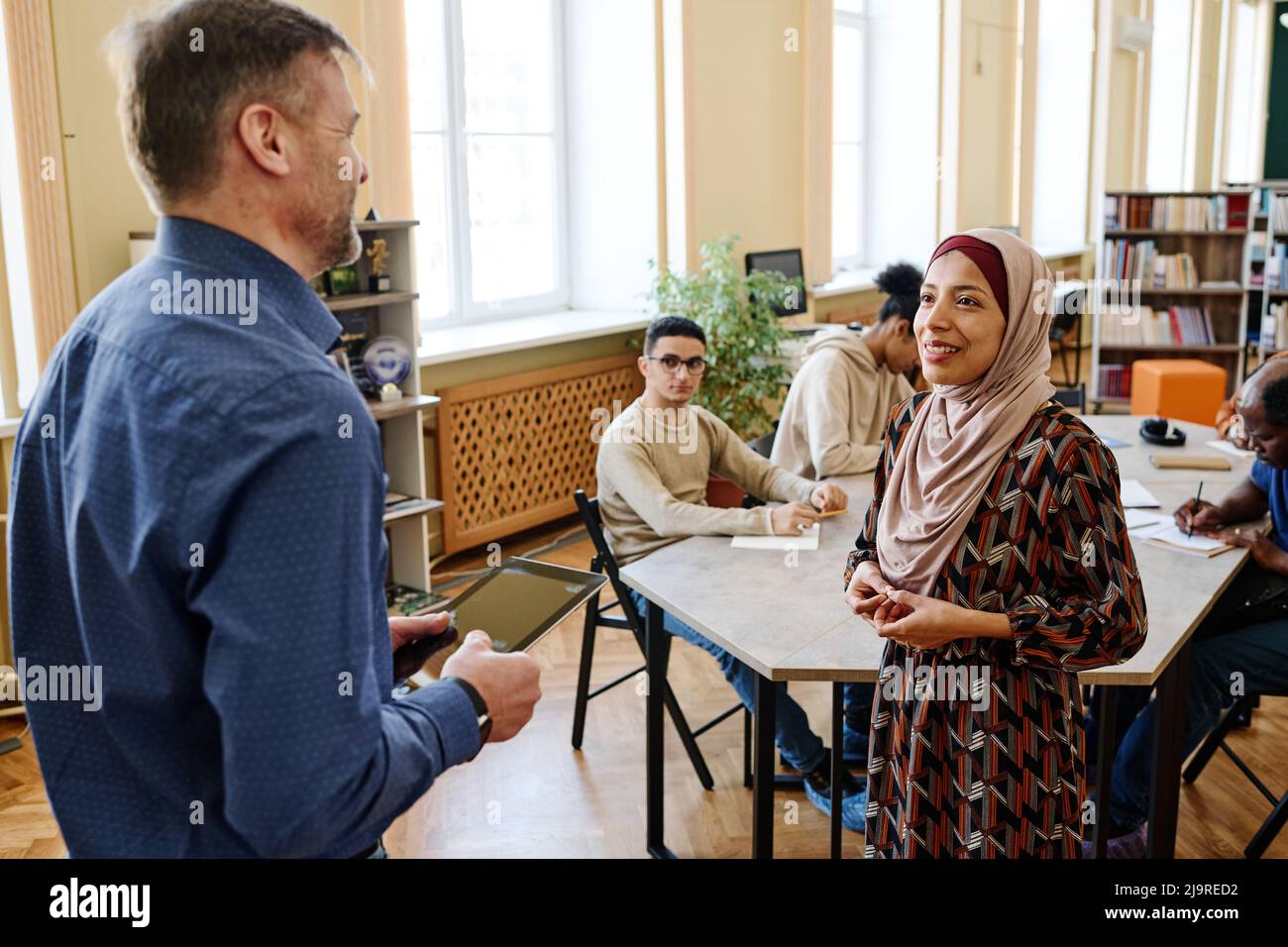 High angle shot of Muslim woman attending classes for immigrants standing in front of teacher trying to speak English Stock Photo