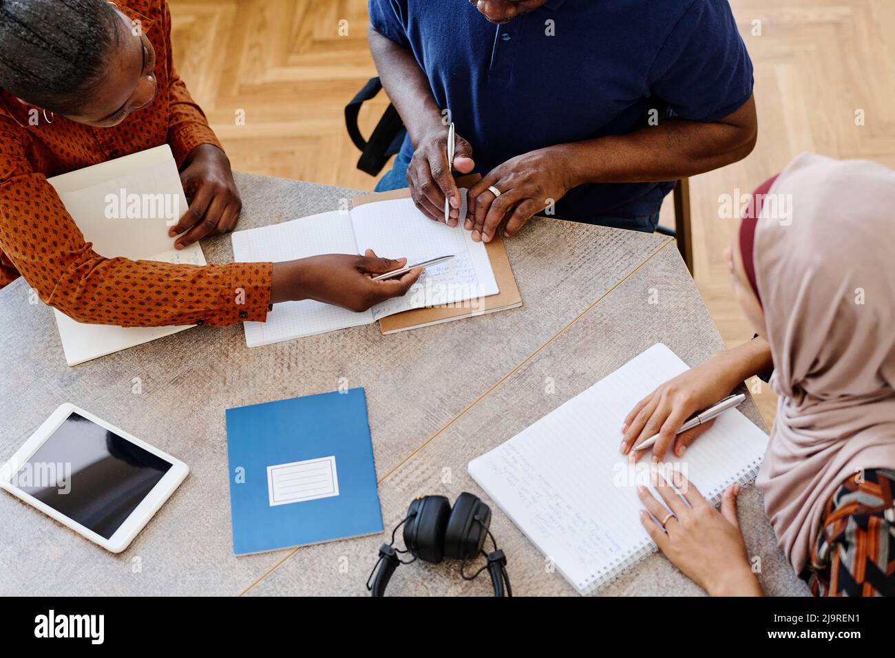 High angle view shot of two young women helping mature Black man to correct mistake during English language class for immigrants Stock Photo