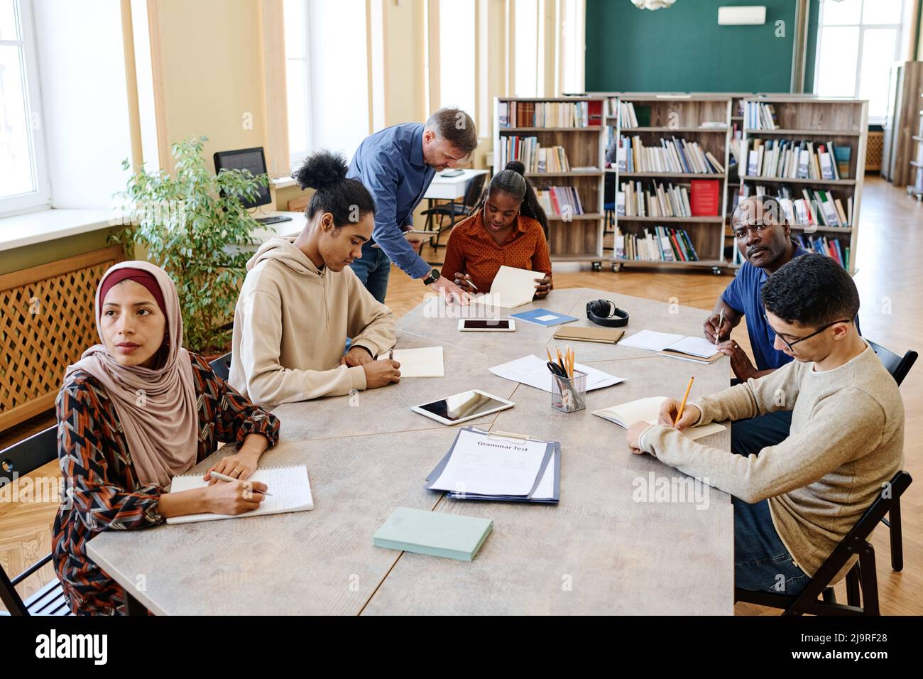 High angle view shot of mature teacher working with multi-ethnic group of immigrant students in library Stock Photo