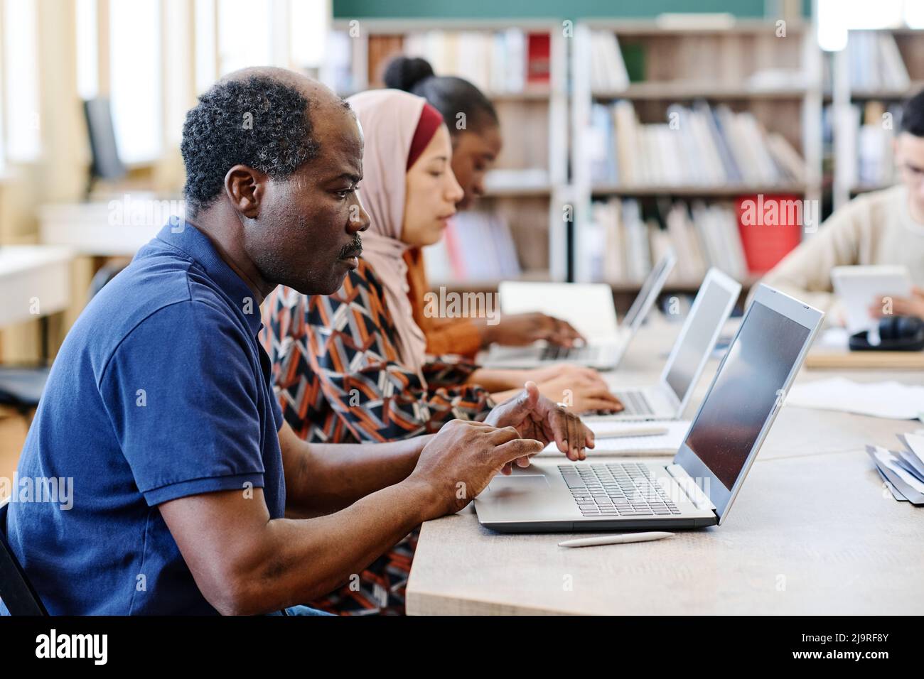 Group of ethnically diverse immigrant students wokring on laptops during lesson searching for information in Internet Stock Photo